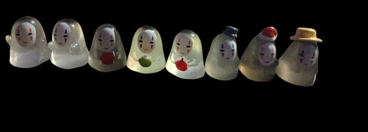 Row of glass figurines with various facial expressions and accessories on a black background