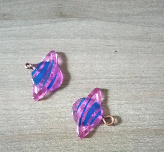 Two pink and purple glass fish-shaped charms on a textured surface