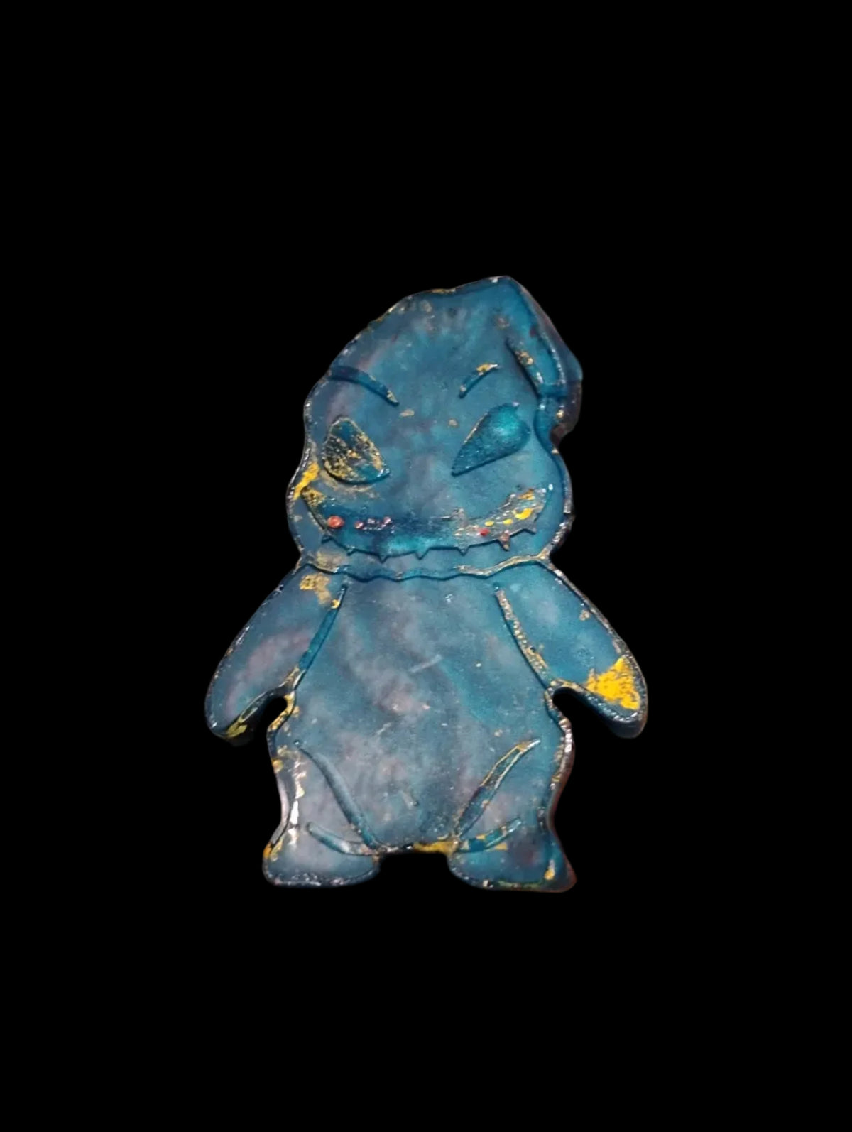 A small blue and gold decorative figurine or ornament lying on a brown textured carpet, with a person's fingers visible at the bottom edge.
